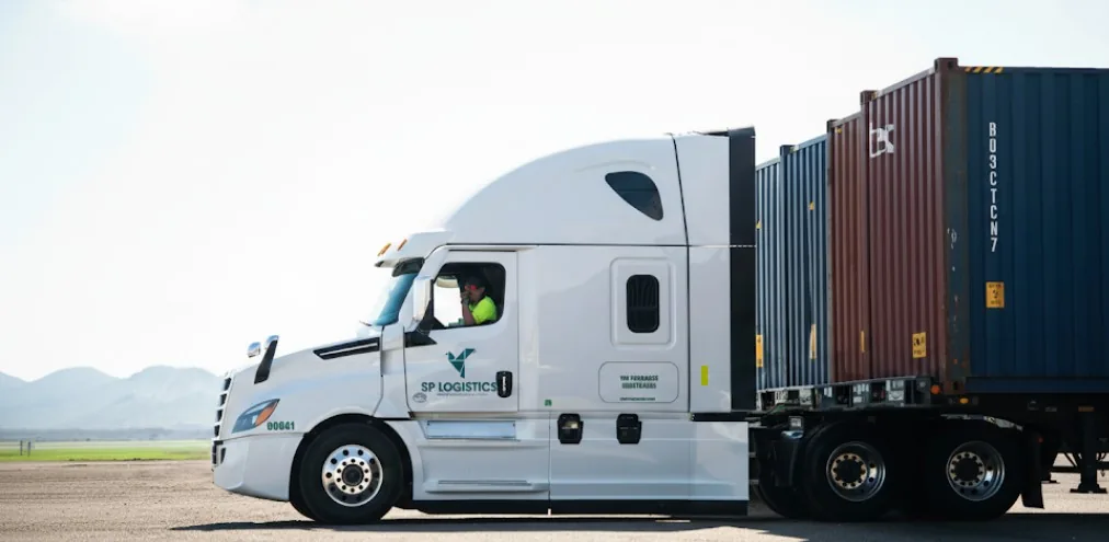 Driver in a white SP Logistics tractor hauling an ocean container